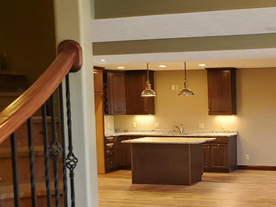 A completed basement that Houston Remodel Service did that includes kitchen features like a kitchen island and sink with faucet, as well as hanging lights.