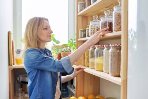 A woman checks her shelf to see her jars filled with various foods.